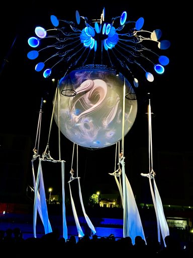 Installation artistique nocturne avec une sphère illuminée et des drapés, créant une ambiance mystique.