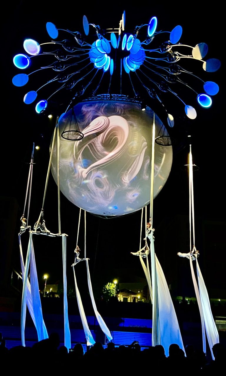 Installation artistique lumineuse avec un dragon blanc, projection video monumentale suspendu et éléments en tissu flottant.