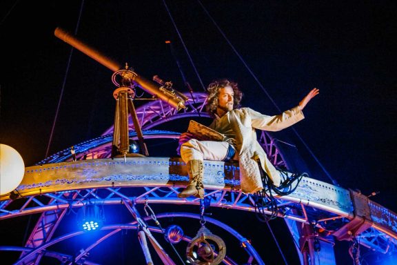 Un personnage suspendu sur une structure métallique, pointant vers le ciel avec un télescope.