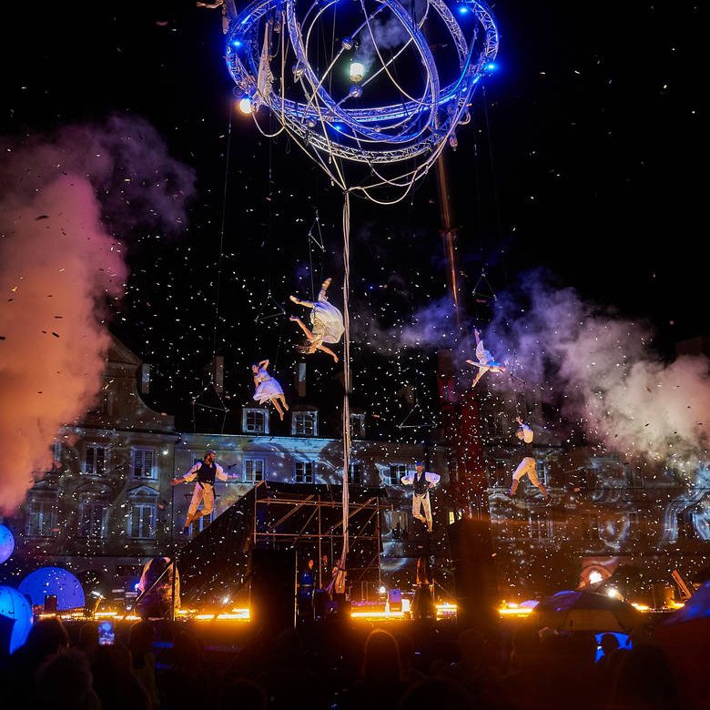 Spectacle nocturne avec des artistes en spectacle, effets de lumière et feux d'artifice.