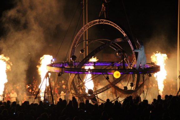 Un spectacle nocturne avec des flammes, une structure en mouvement et une foule émerveillée.