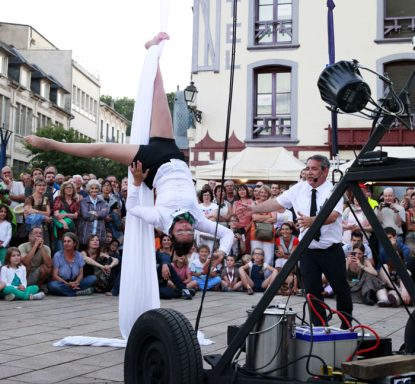 Artiste équilibriste en costume blanc, exécutant un numéro acrobatique devant une foule.