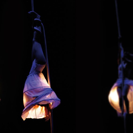Danseuse en suspension, vêtue d'une robe blanche, éclairée par une lumière douce.