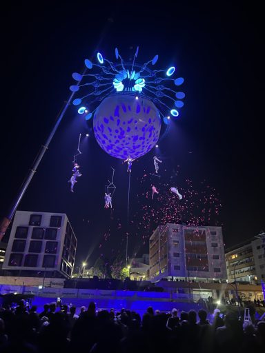Spectacle nocturne avec des artistes suspendus, des feux d'artifice et des lumières colorées.