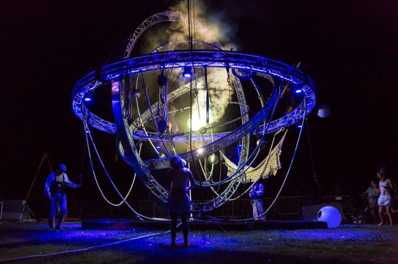 Installation lumineuse artistique avec des figures humaines sous un ciel nocturne.