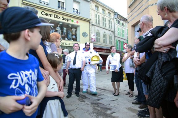 Groupe de personnes rassemblées autour d'un personnage déguisé en marin dans une rue animée.