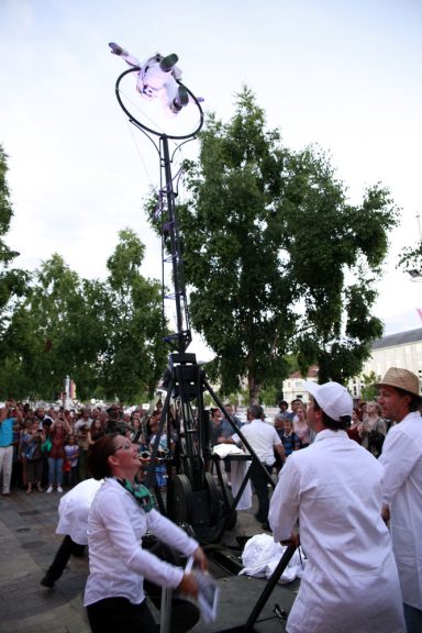 Artiste de rue performe au sommet d'une structure, entouré de spectateurs fascinés.
