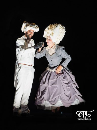 Deux artistes en costumes historiques, l'un en blanc et l'autre en robe grise.