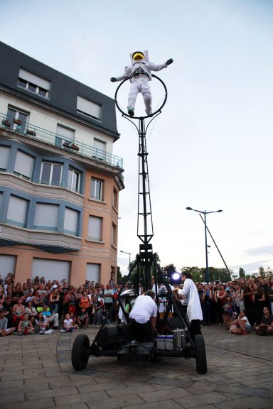Un artiste de cirque effectue un numéro en hauteur sur un monocycle, devant une foule.