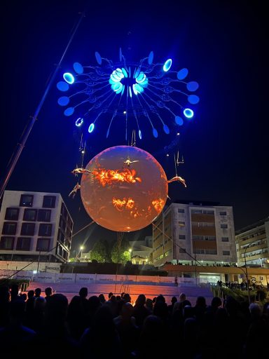 Spectacle nocturne avec une sphère lumineuse et des feux d'artifice au-dessus d'une foule.