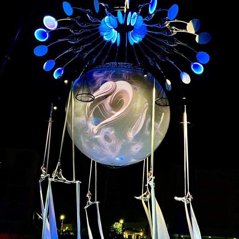 Sculpture lumineuse avec sphère flottante et éléments suspendus, à l'ambiance nocturne.