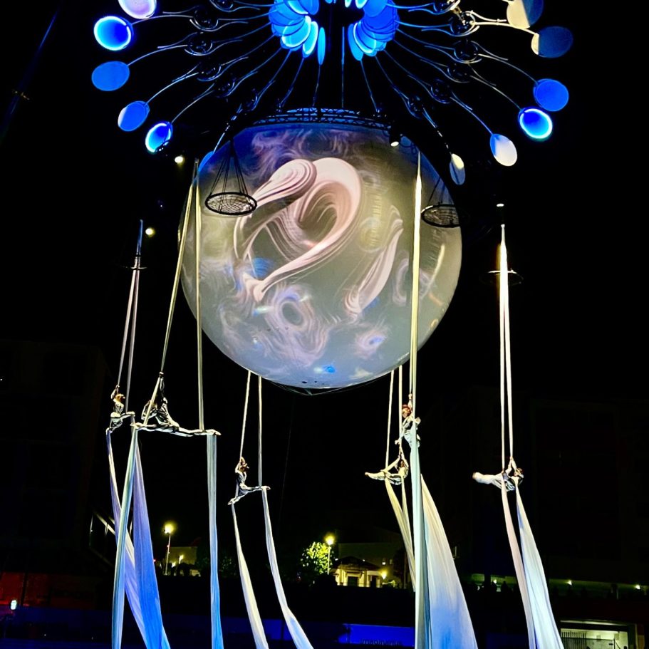 Une scène artistique nocturne avec une grande sphère suspendue et des éléments aériens.