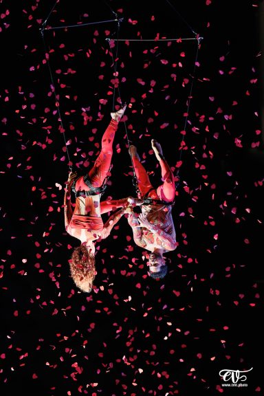 Deux artistes en performance acrobatique, entourés de confettis colorés.