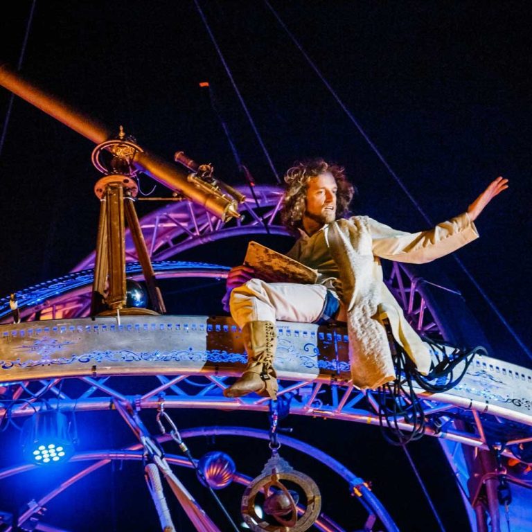 Une personne en costume navigue sur une structure de spectacle illuminée la nuit.