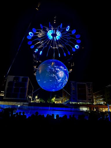 Projection d'une Terre en apesanteur sous un ciel nocturne illuminé par des lumières bleues.
