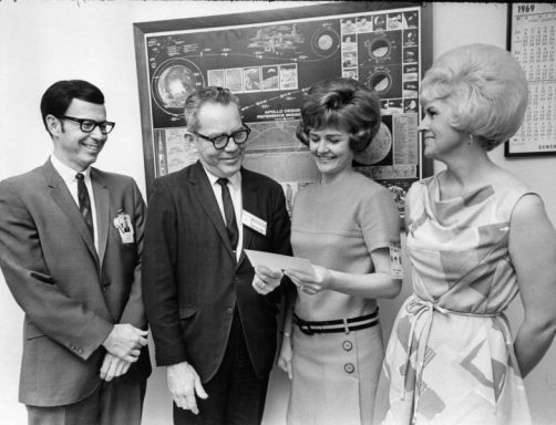 Quatre personnes souriantes, discutant autour d'un document, dans un cadre formel.