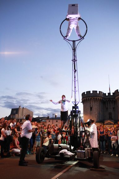 Un artiste sur une plateforme élévée, entouré d'un public, devant un château.