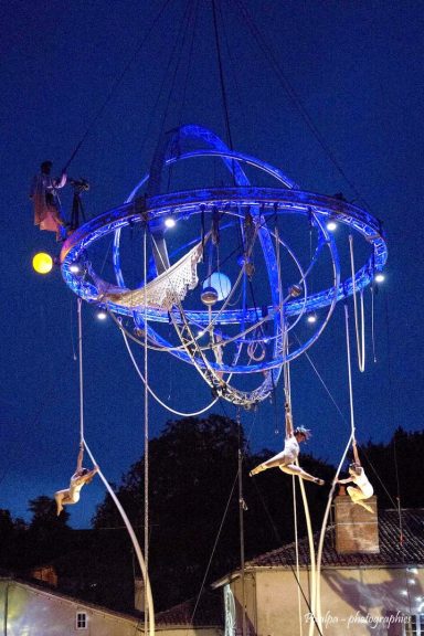 Artistes de cirque effectuant des acrobaties suspendues sous un grand cercle lumineux.