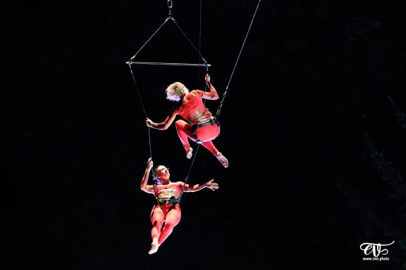 Deux artistes de cirque effectuent des acrobaties suspendues dans les airs.