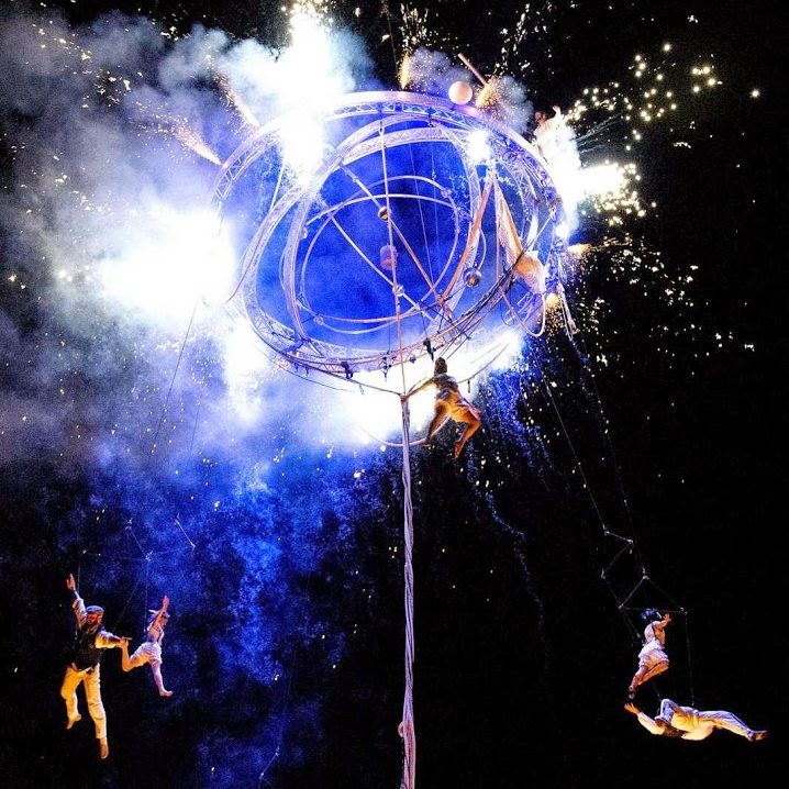 Des acrobates en pleine performance autour d'une sphère lumineuse et étincelante.