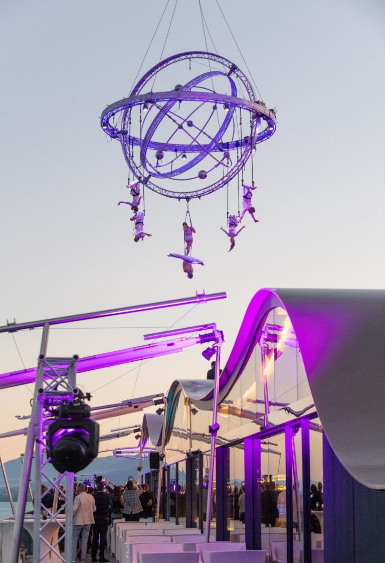 Installation artistique suspendue avec des performances aériennes, lumière violette ambiante.