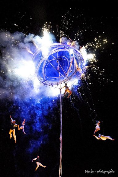 Performers acrobatically climbing a tall structure surrounded by colorful sparks.