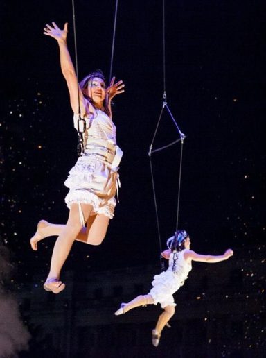 Deux artistes en suspension dans les airs, vêtues de costumes scintillants.