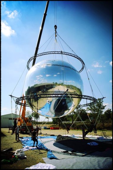 Installation d'une grande sphère réfléchissante avec des ouvriers et une grue.