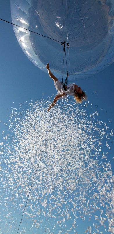 Enfant suspendu dans une bulle, lâchant des confettis blancs dans un ciel bleu.