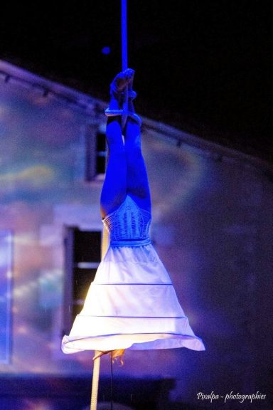 Une personne suspendue à un fil, vêtue d'une robe blanche et bleue.