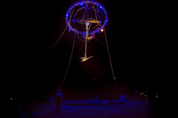 Artiste acrobatique suspendu dans les airs, éclairé par des lumières colorées.