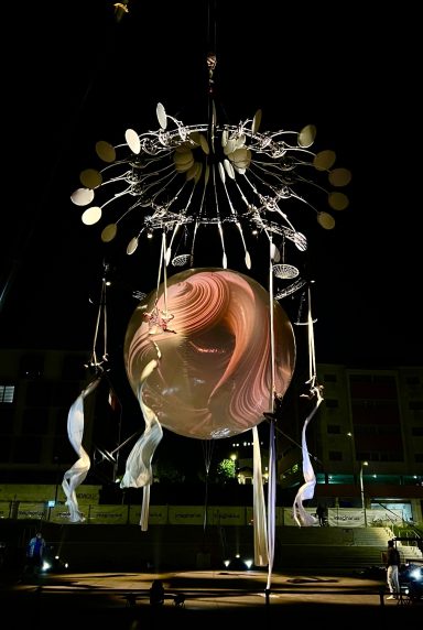 Sculpture nocturne avec un globe lumineux et des éléments suspendus.