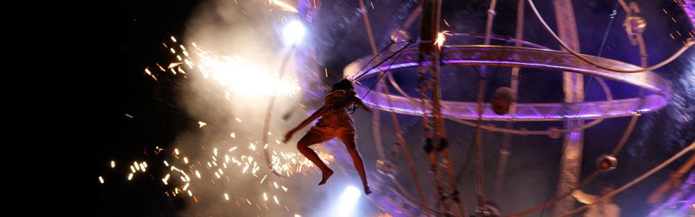 Artiste acrobatique suspendu dans un cadre illuminé par des éclats lumineux.