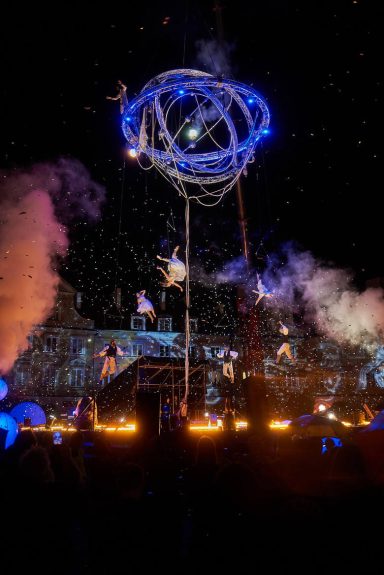 Installation artistique nocturne avec des effets de lumière et de la pyrotechnie.