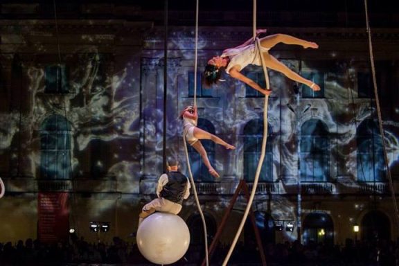 Acrobates suspendus exécutant des performances sous un fond illuminé et artistique.