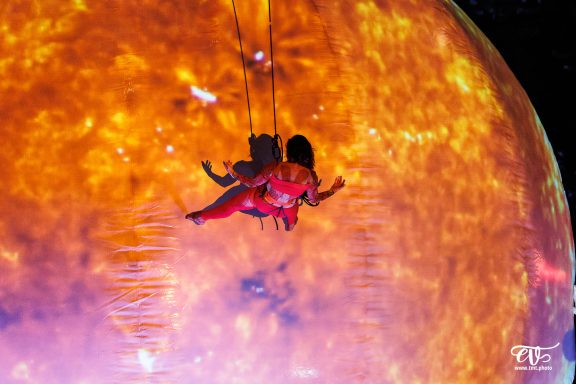 Une silhouette suspendue devant un grand écran représentant le soleil.