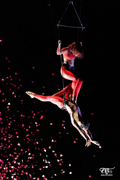 Deux artistes acrobates suspendus, en apesanteur, avec des confettis au sol.