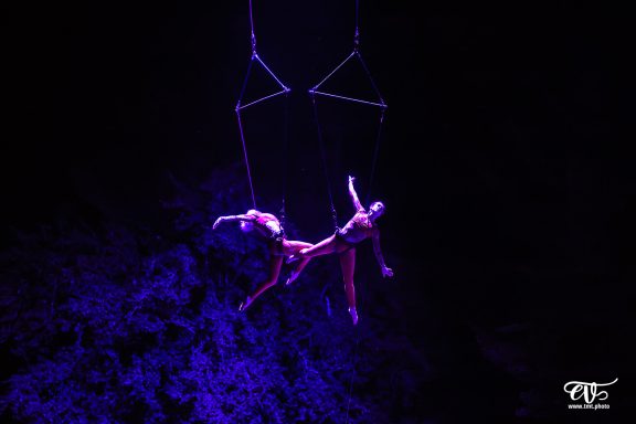Deux artistes suspendus en hauteur, effet dramatique de lumière violette en arrière-plan.