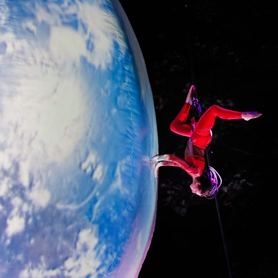 Un grimpeur en tenue spatiale s'accroche à une sphère représentant la Terre.
danse pendulaire
