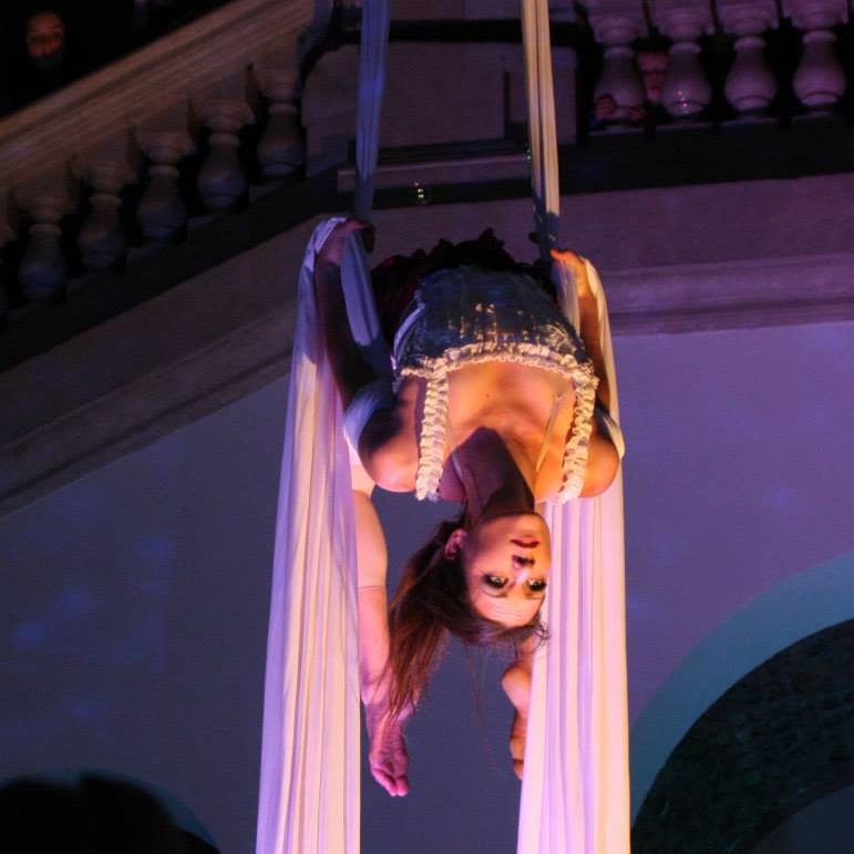 Artiste de cirque suspendue, effectuant une performance aérienne avec des tissus.